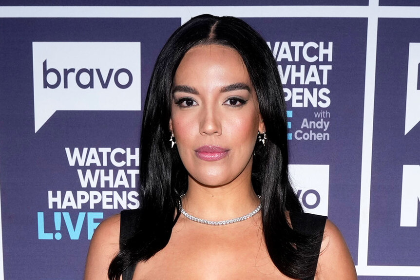 Danielle Olivera wearing a black gown in front of a step and repeat at the Watch What Happens Live clubhouse in New York City.