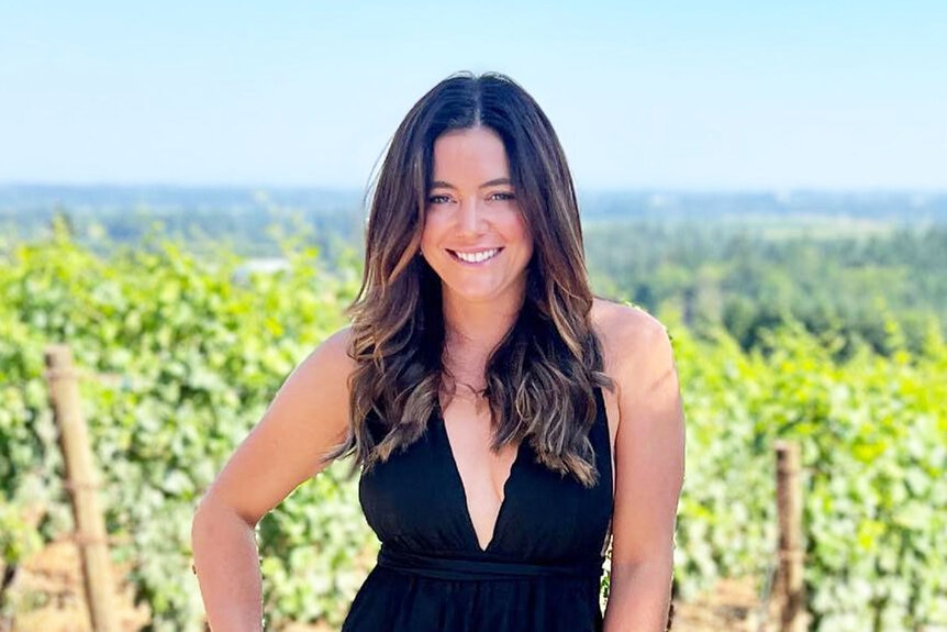 Malia White smiling in front of a vineyard in Portland, Oregon.