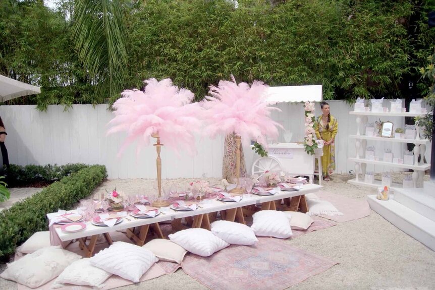 Pink table decorations with floor pillows sit in a lush backyard.
