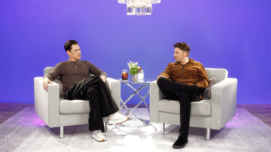 Tom Sandoval and Tom Schwartz sitting on armchairs and talking in front of a backdrop.