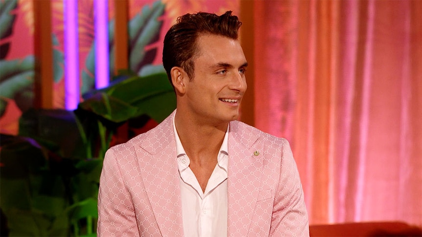 James Kennedy smiling in a pink suit in front of plants and curtains.