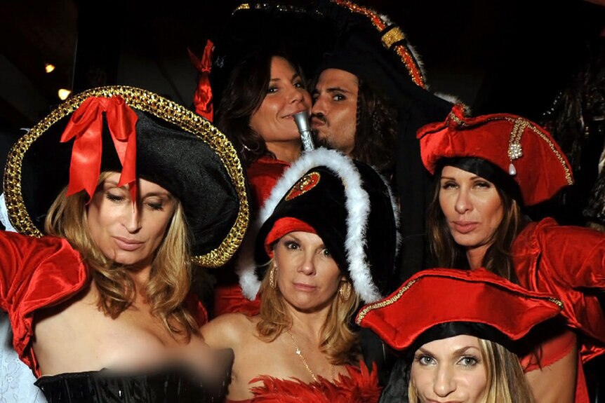 The cast of Real Housewives of New York wearing red outfits and partying with a pirate.