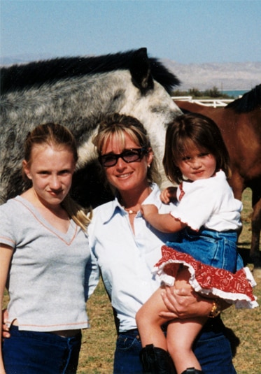 Kim Richards standing in front of horses with two of her daughters.