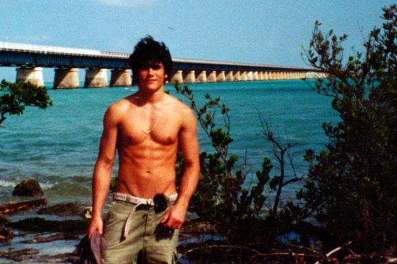 Tom Sandoval poses in front of a bridge shirtless.