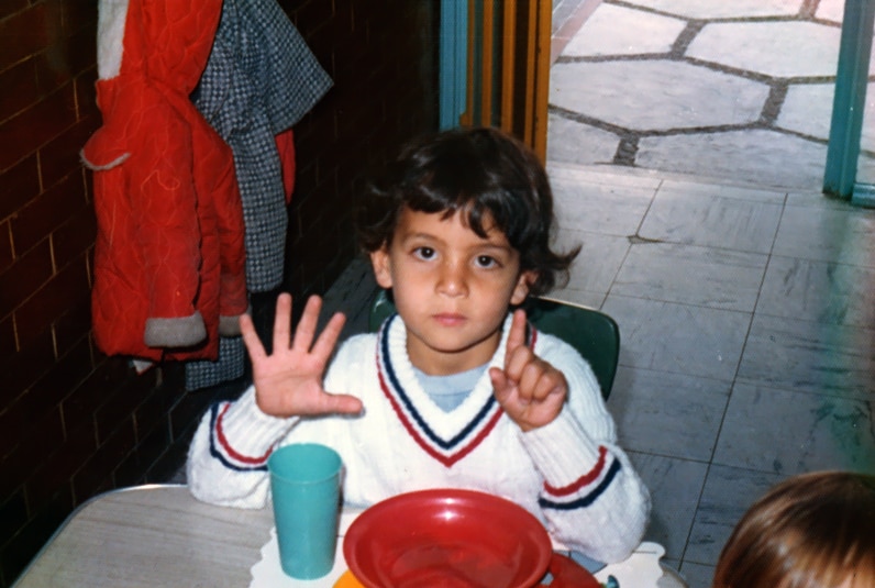 Mauricio Umansky holding up 6 fingers as a little boy sitting at a table.