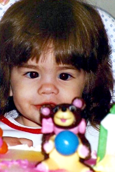 Katie Maloney as a little girl plays with a toy in front of her face.