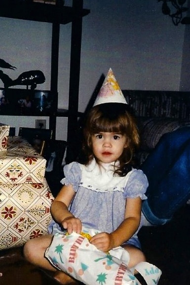 Katie Maloney opens up a present and wears a party hat as a young girl.