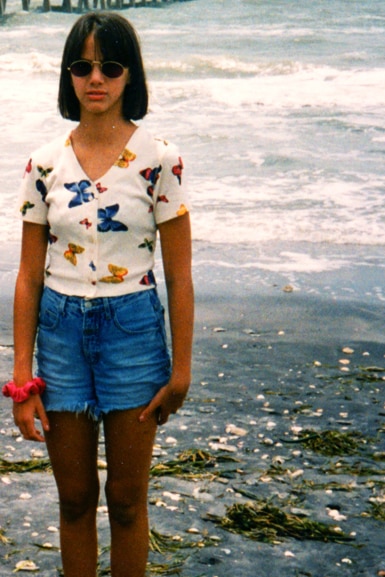 Kristen Doute wears a butterfly top and denim shorts while standing at the beach.