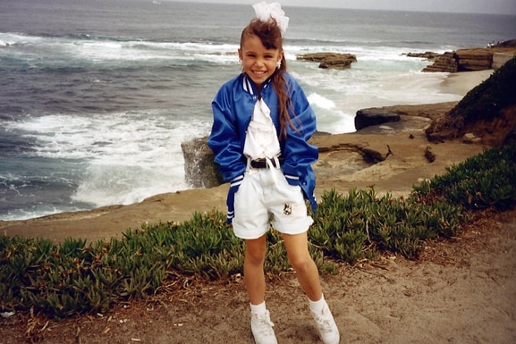Scheana Shay smiles in front of the ocean while wearing a windbreaker.