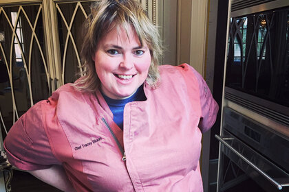 Tracey Bloom wearing a pink chef's jacket in a kitchen.