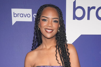 Riley Burruss smiling with braids in front of the Bravocon 2022 step and repeat.