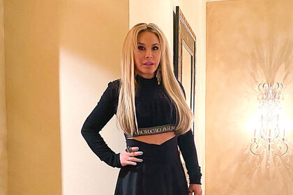 Adrienne Maloof posing in front of a wall and sconce in a black outfit.