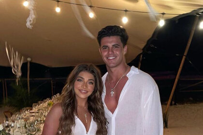 Gia and Christian pose together in all white on a beach.