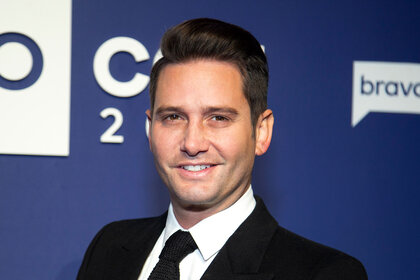 Josh in a suit smiling in front of a blue step and repeat.