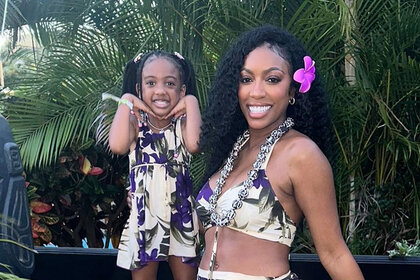 Porsha Williams and Pilar Jhena pose in coordinated tropical outfits in front of palm trees.