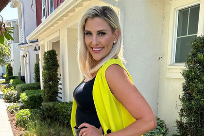 Gina Kirschenheiter smiling and posing in a black outfit with neon yellow in front of a building.