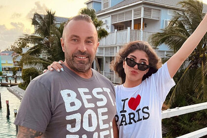 Joe and Milania pose together in t-shirts outdoors during a sunset.