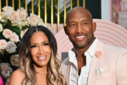 Sheree Whitfield and Martell Holt smile together in front of a pink and gold display.