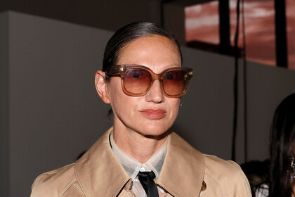 Jenna Lyons with her hair slicked back wearing brown, translucent, sunglasses and a beige coat with a sheer, white, top and black tie at Rosie Assoulin NYFW presentation.