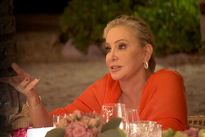 Shannon Storms Beador wearing a red shawl and sitting at a table while out to dinner with her RHOC castmates.