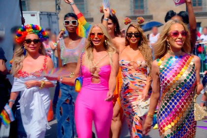 RHOM Season 6 cast at a street festival wearing bright colors and waving the PRIDE flag.