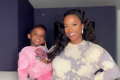 Kandi Burruss holding Blaze Tucker while smiling together in front of a purple wall.