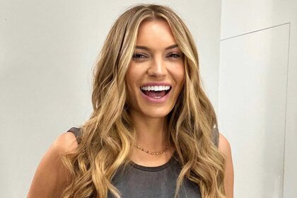 Lindsay Hubbard laughing in a dark gray tank top in front of a white wall.