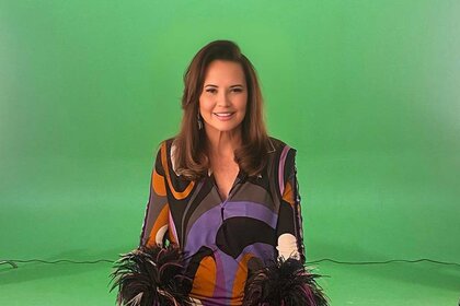 Patricia Altschul sitting and smiling in front of a green screen.