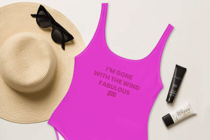 A neon pink swimsuit next to a straw hat, sunglasses, and beauty products.