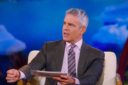 Andy Cohen talking and sitting in front of a backdrop.