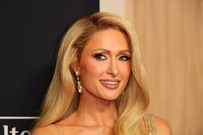 Paris Hilton smiling in front of a step and repeat.
