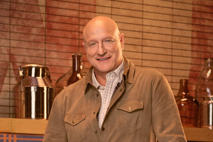 Tom Colicchio wearing a brown top in a food pantry