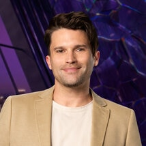 Tom Schwartz wearing a beige jacket and white t-shirt while in a purple room overlooking LA.