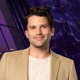 Tom Schwartz wearing a beige jacket and white t-shirt while in a purple room overlooking LA.
