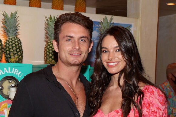 James and Ally smiling in front of a row of pineapples at an event.