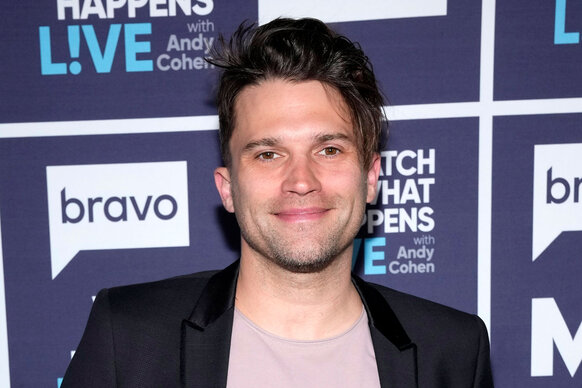 Tom Schwartz wearing a tee shirt and black blazer in front of the WWHL step and repeat.
