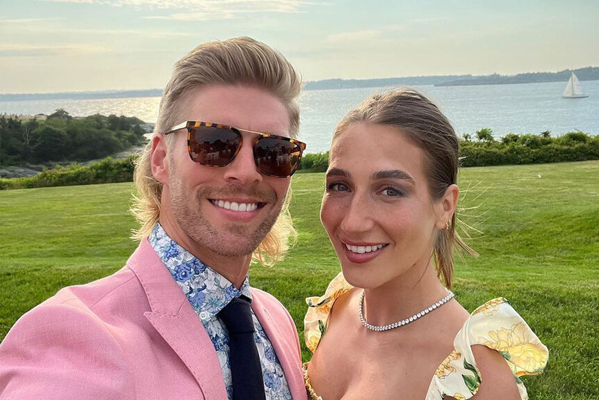Kyle Cooke and Amanda Batula posing together in front of the Newport, Rhode Island coastline.
