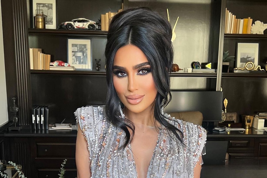 Lilly Ghalichi posing in an office in full glam and a cocktail dress.