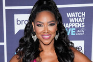 Kenya Moore smiling in a pink dress in front of the WWHL step and repeat.