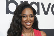 Kenya Moore wearing a red jumpsuit on a step and repeat at BravoCon 2023.