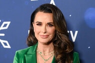 Kyle Richards posing in a green blazer in front of a step and repeat.