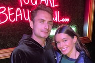 James Kennedy and Ally Lewber smiling together in front of a neon sign.
