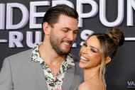 Scheana Shay and Brock Davies laugh and embrace each other in front of a step and repeat.