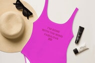 A swimsuit with a quote on it next to skincare, a hat, and sunglasses.