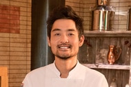 Soo Ahn smiling in his chef uniform inside of a pantry.