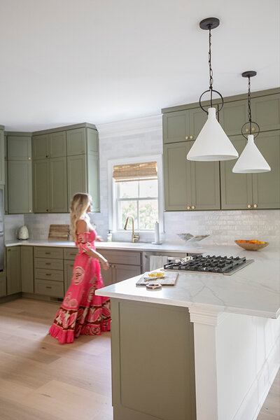 Madison wearing a pink dress while in her kitchen with a peninsula and pendant lights.
