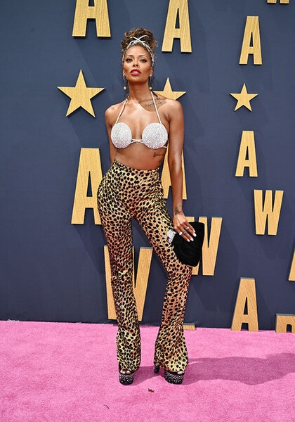 Eva Marcille posing on a red carpet wearing a sparkling bra top and cheetah print pants.