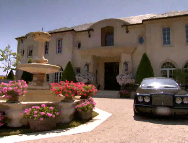 The exterior of Lisa’s first Tuscan-style home with a large fountain with flowers and a black luxury car.