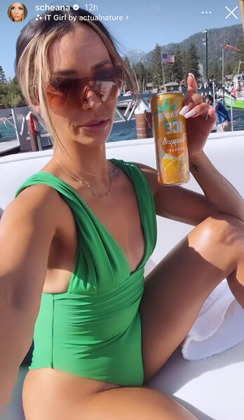 Scheana holding a can and wearing a green one-piece swimsuit and sunglasses on a boar.