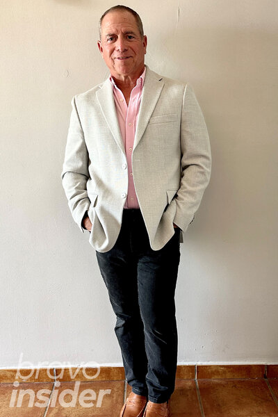 Glenn in a pink button down, light beige suit jacket, black pants and caramel toned loafers.